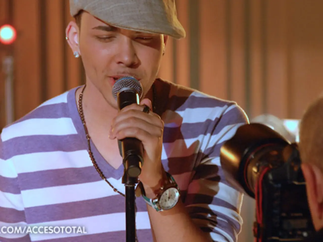 In this image there is a person wearing a cream color hat holding a microphone , and singing a song...