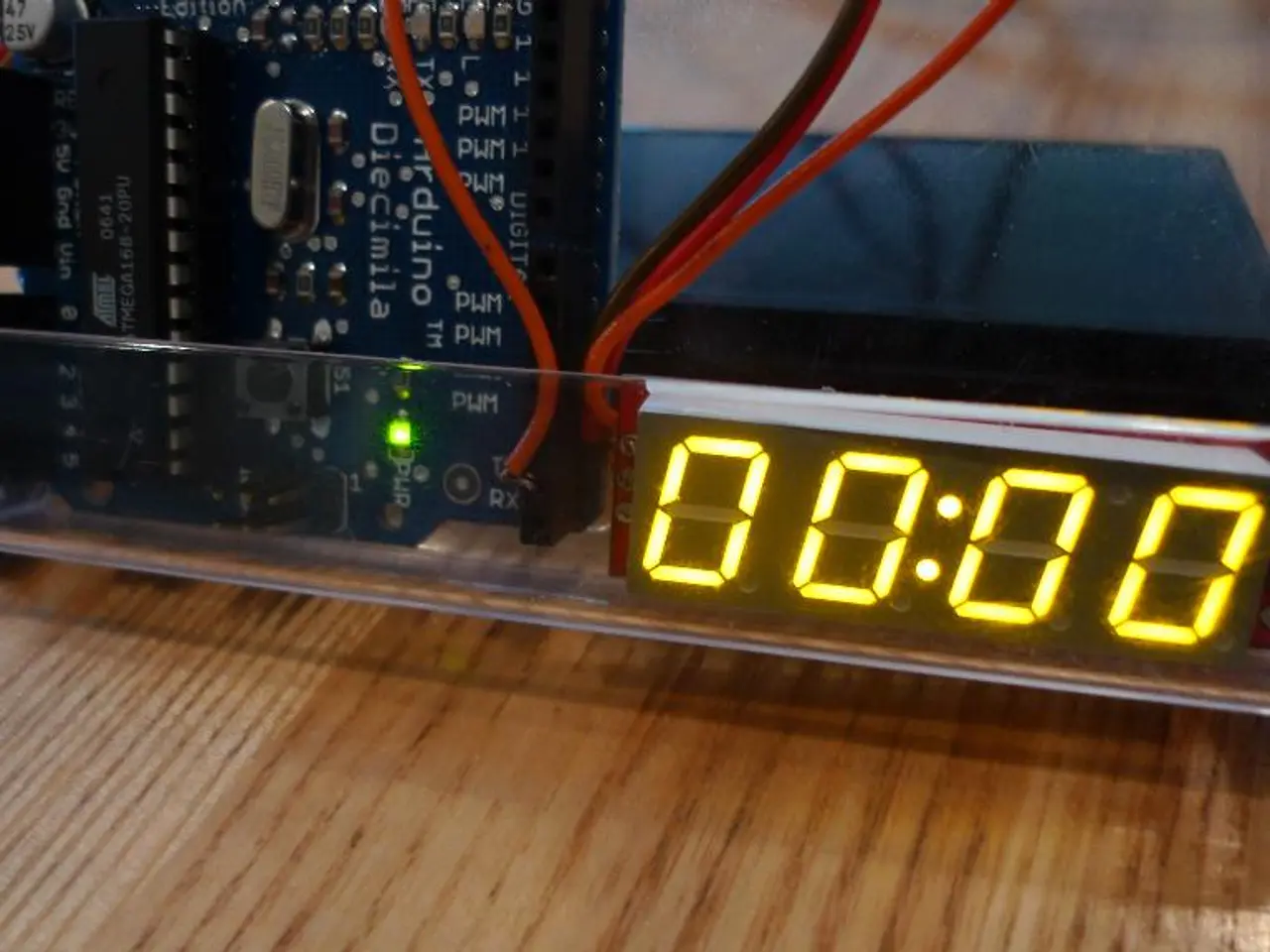 In this image there is a glass tray on a wooden surface. In the tray there are digital display...