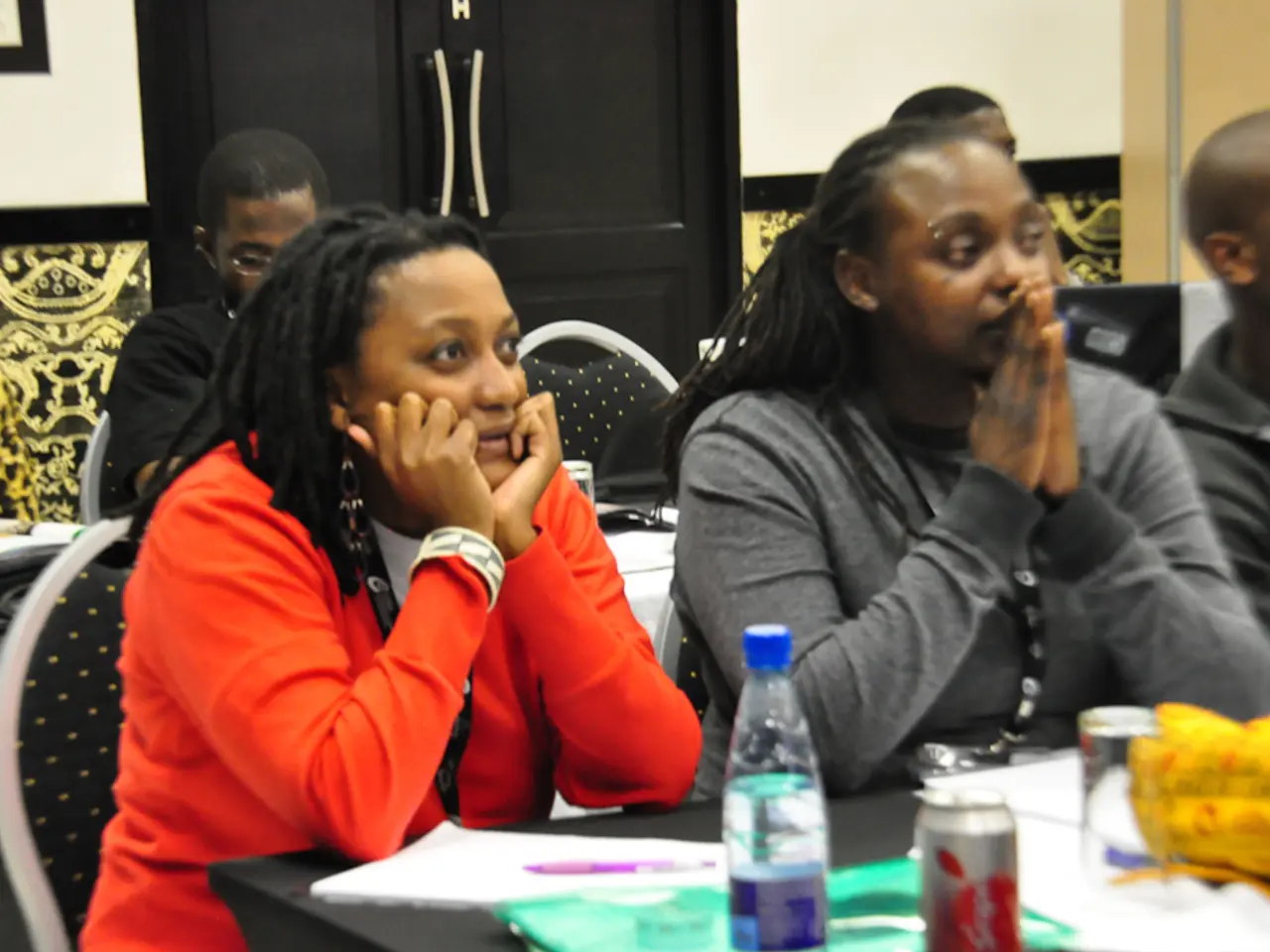 In the image we can see there are people sitting on chair and on table there is a water bottle,...