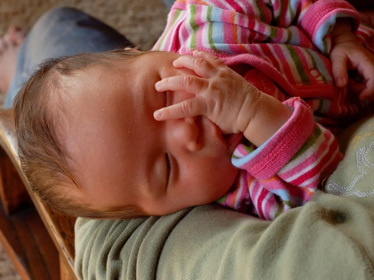 In this picture we can see a person sitting and holding a child, this child is sleeping, at the...