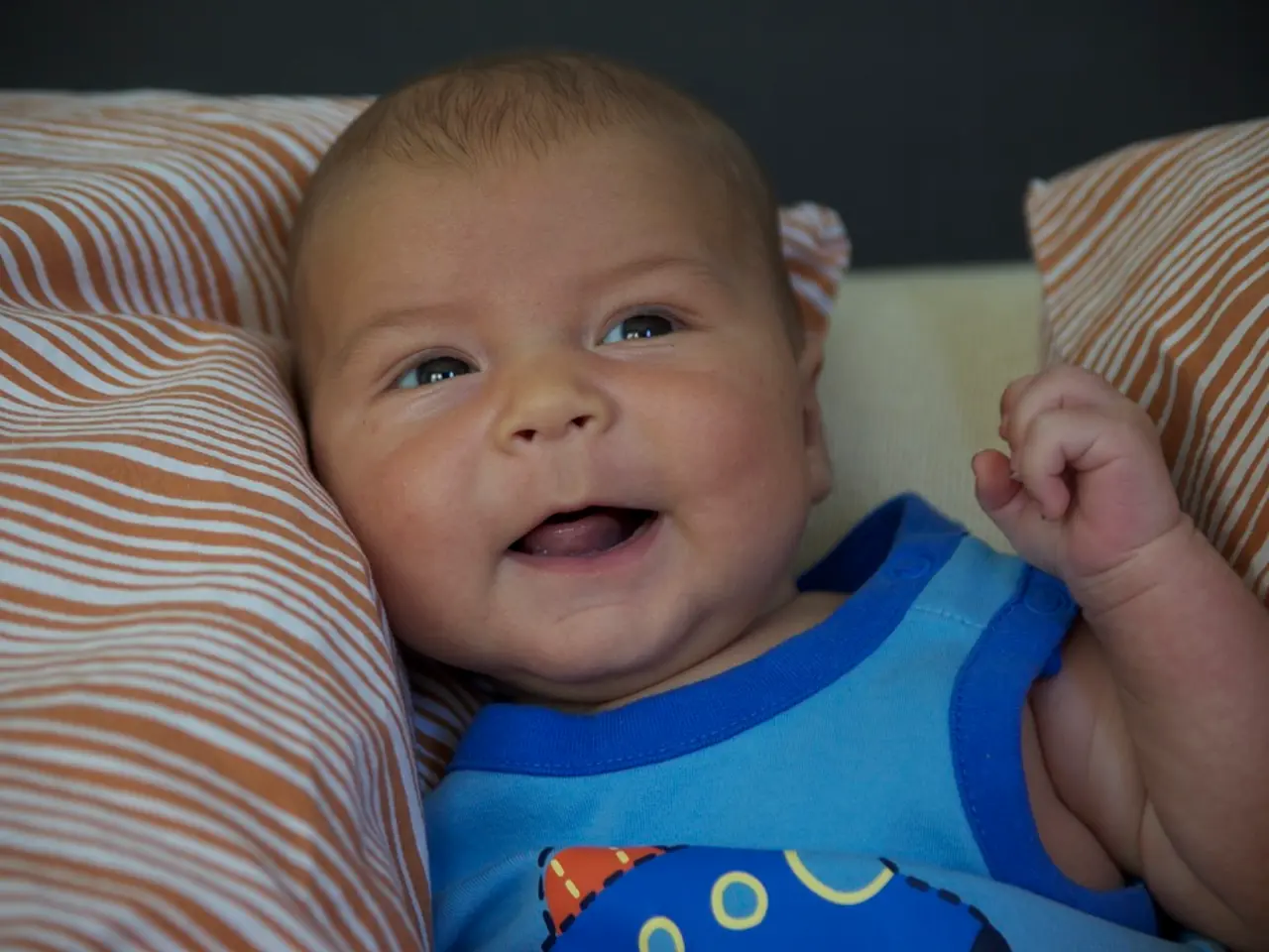 Here I can see a baby wearing a blue color t-shirt and laying on the bed. On both sides of the...