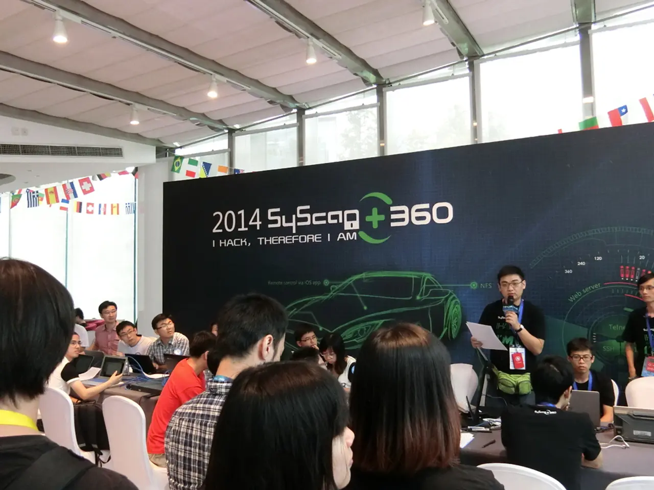 There are group of people sitting on the chairs. Here is the man standing,holding mike and talking....