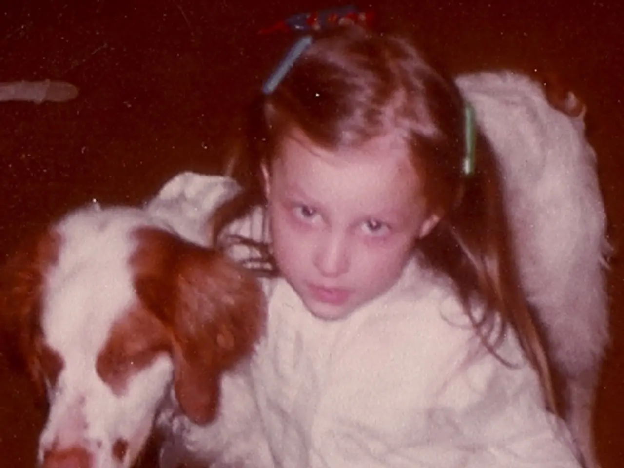 In this picture we can see a girl who is sitting on her knees. And there is a dog.