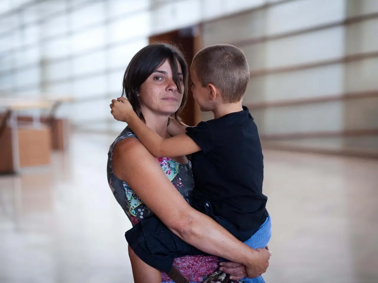 In the image we can see there is a woman standing in the building and she is carrying a kid. Behind...
