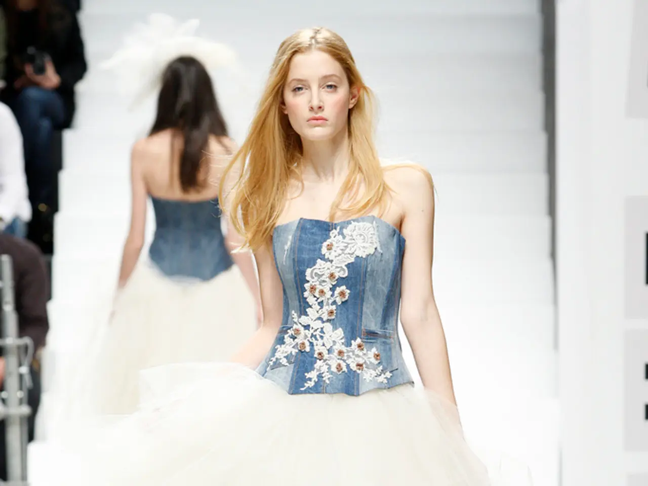 Here in this picture we can see two women walking on the ramp with some designer clothes over a...