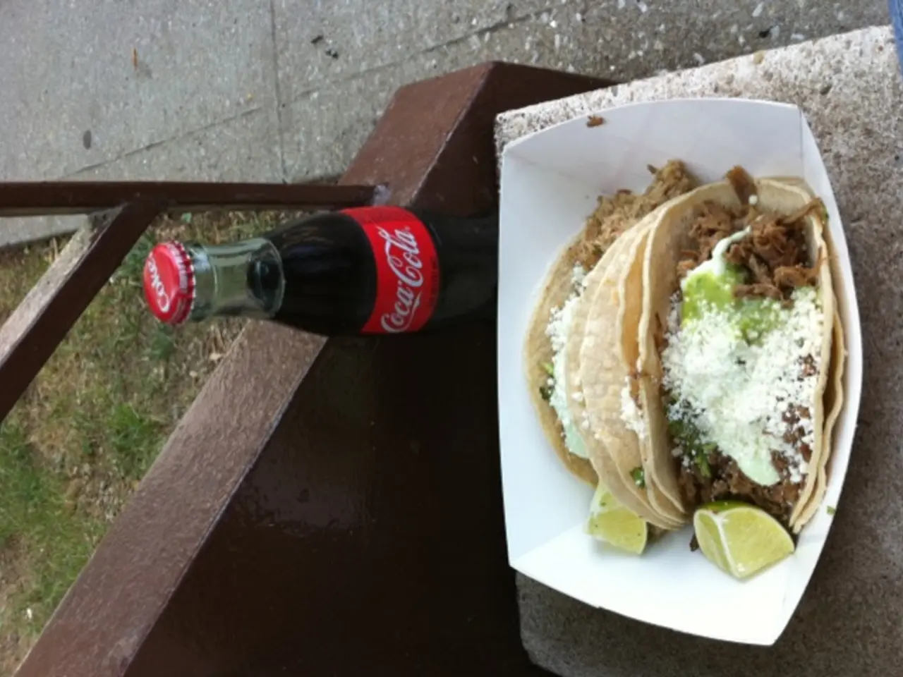 There is a snack item kept on a bench and behind the snack there is a cold drink bottle, behind the...