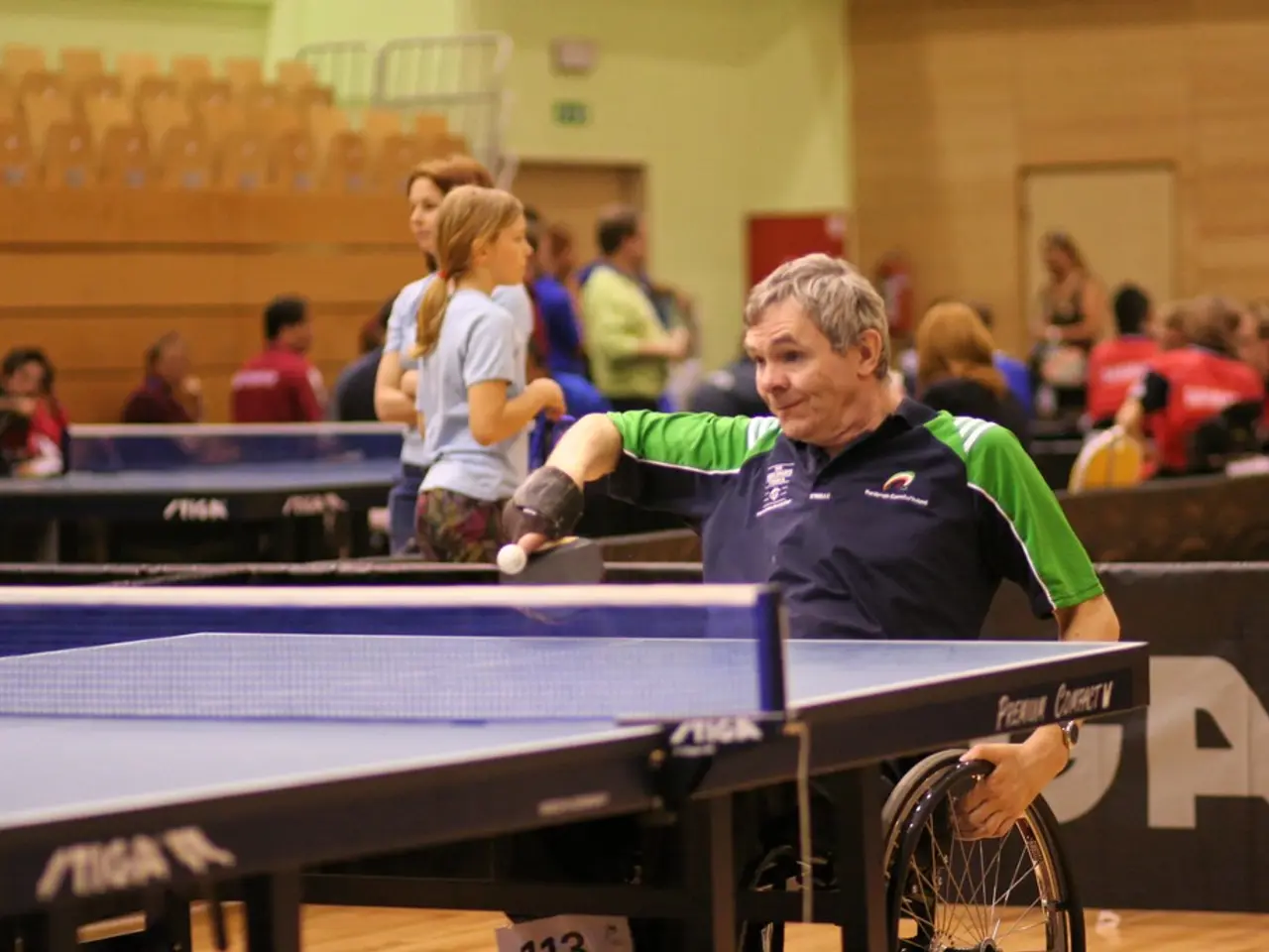 A man who is sitting on the wheelchair is playing table tennis with his hand. In the background we...