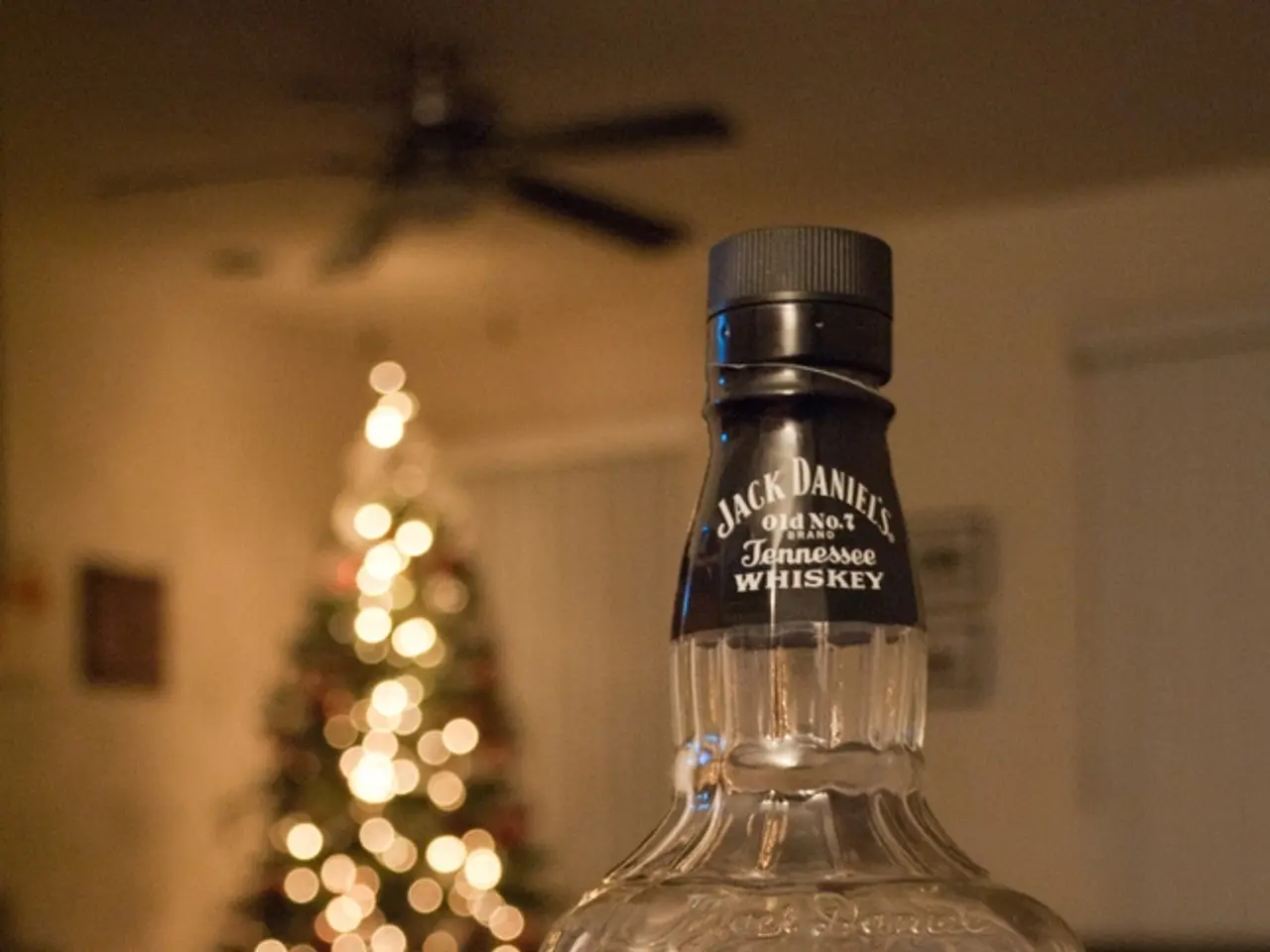 there is a glass bottle on a table on which jack daniels is written. behind that in the room there...