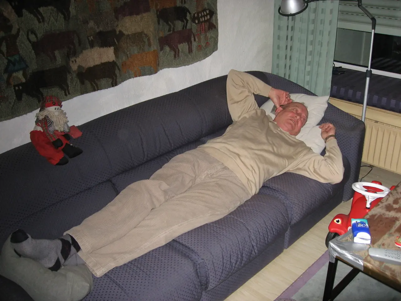 As we can see in the image there is a man sleeping on sofa, a lamp and on the right side there is a...