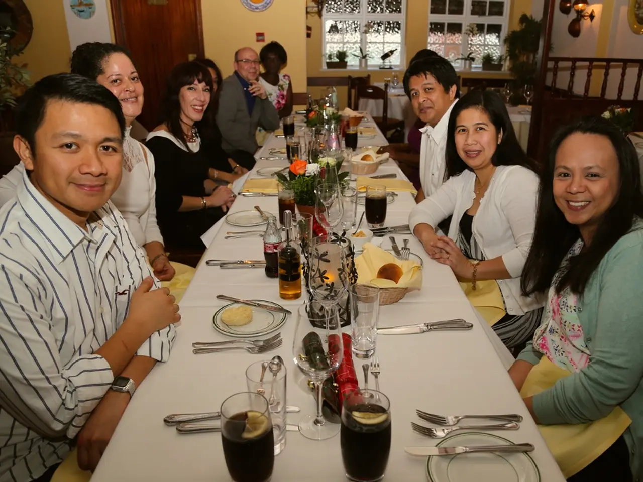 There are group of people sitting around dining table where there are bowls plate spoons knife and...