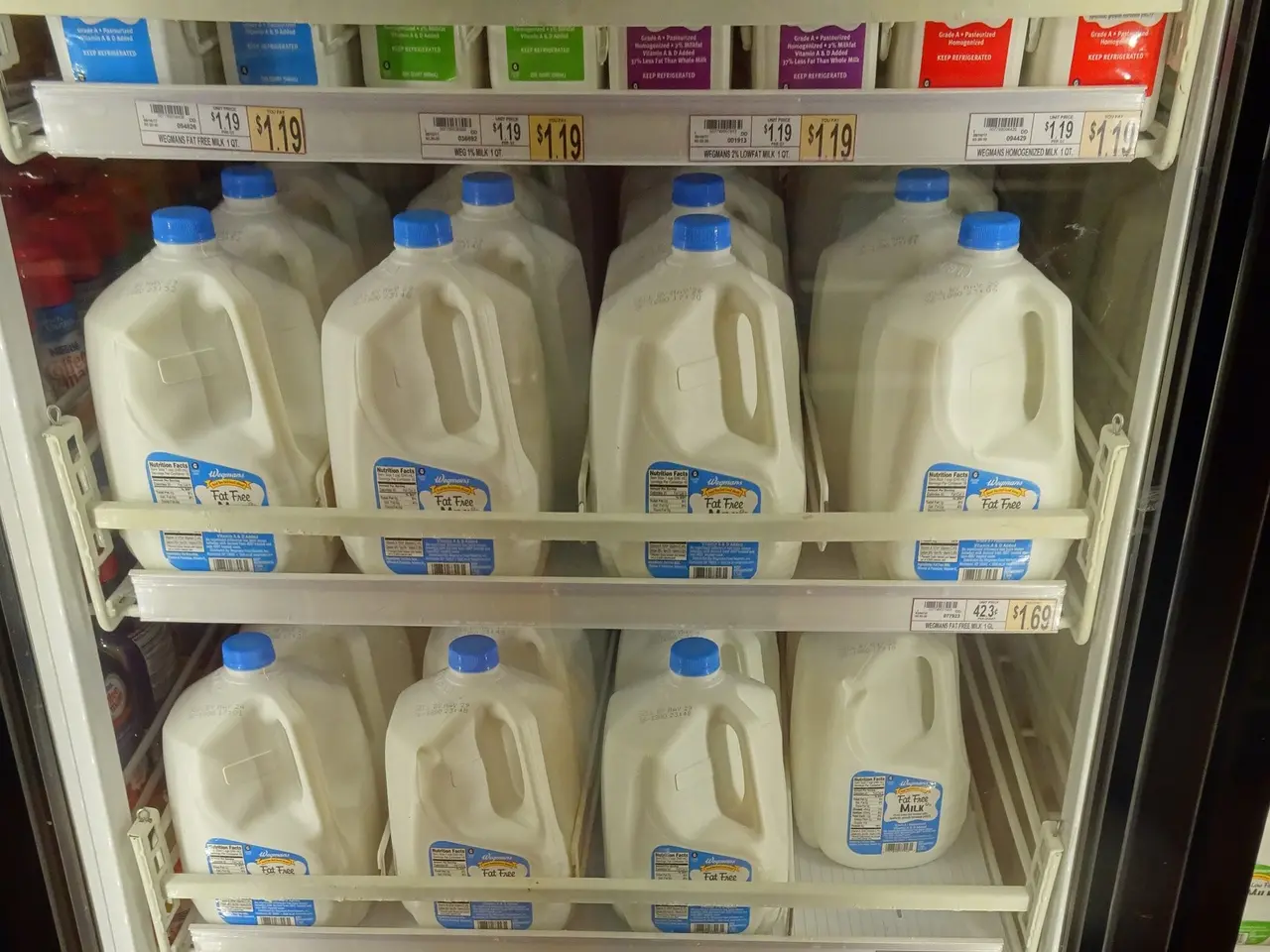 The image shows a refrigerator filled with lots of different types of milk, each with a sticker...