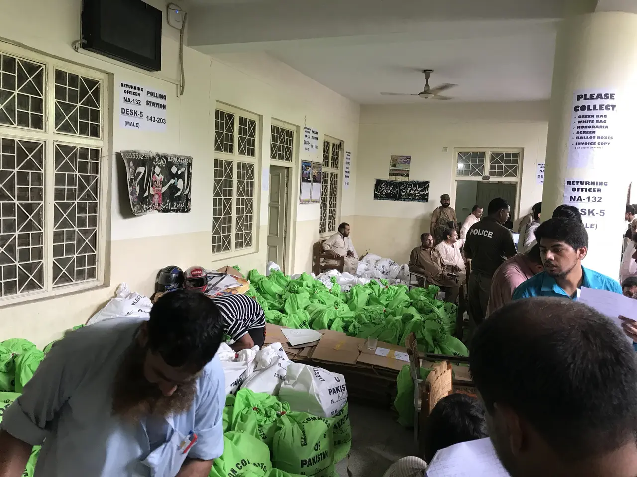 The image shows a group of people standing around a room filled with bags of food. There are people...