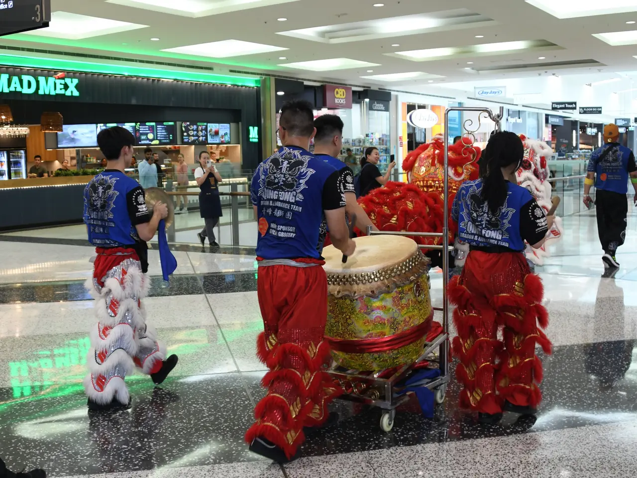 The image shows a group of people in red and blue outfits walking through an airport, with some of...