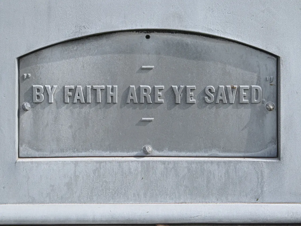 The image shows a plaque on the side of a building that reads "By Faith Are Ye Saved". The plaque...