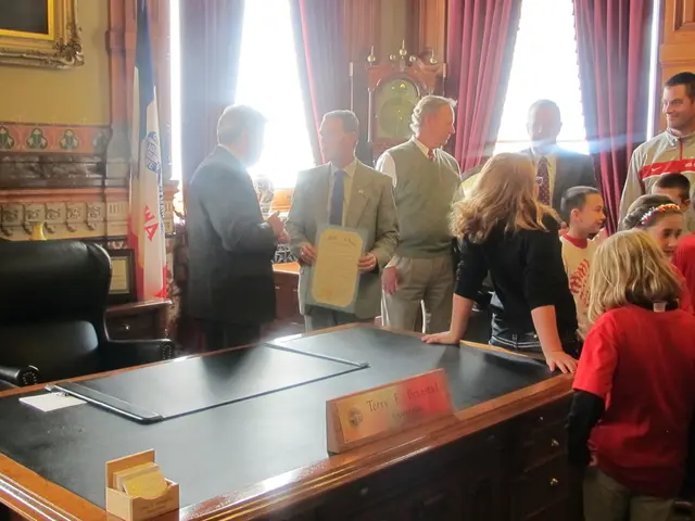 In the image there are few people stood talking and smiling, in the back of them there is a table....