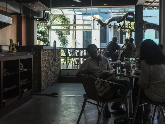This is a cafeteria where we can see group of people sitting on the chairs in front of the tables...