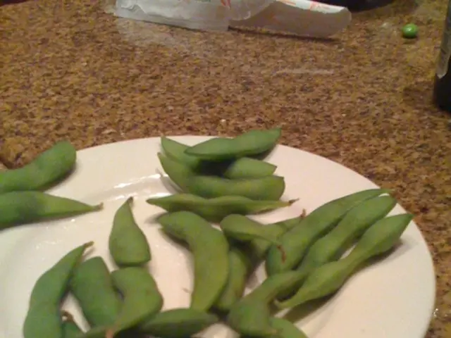 In this image we can see broad bean are kept in a white color plate and the plate is on the brown...