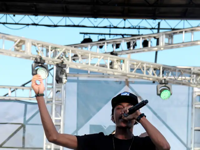 There is a person in black color t-shirt, holding a mic with one hand and standing on a stage....