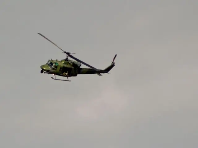 In the picture we can see a helicopter with a fan flying, it is green in color and in the...