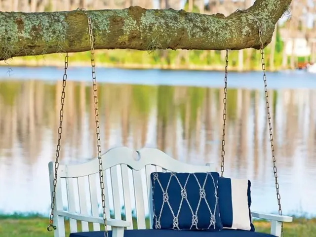 In this image there is a swing which is hanged to the tree stem. Chain is used to hang it. In the...