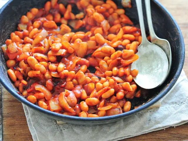In this image, on a wooden surface, there is a cloth on which a black bowl with beans and two...