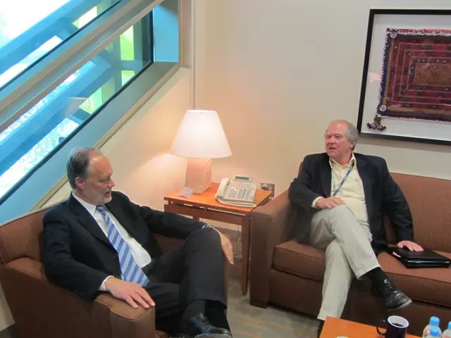In the image there are two old man in suits sitting on sofa with a table beside it along with a...