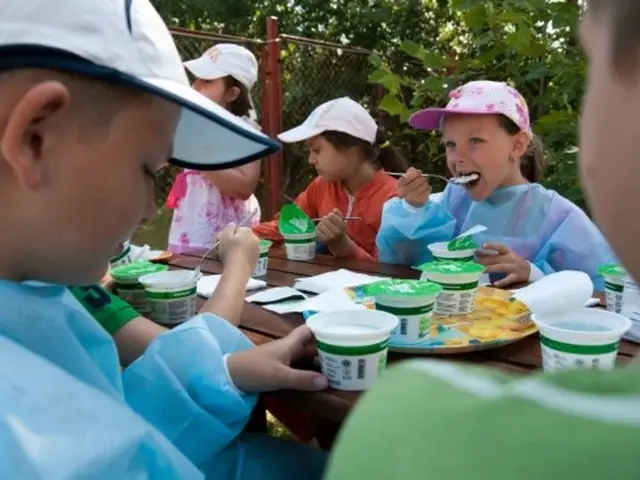 people are sitting. the person at the left is eating. on the table there are cups. behind them...