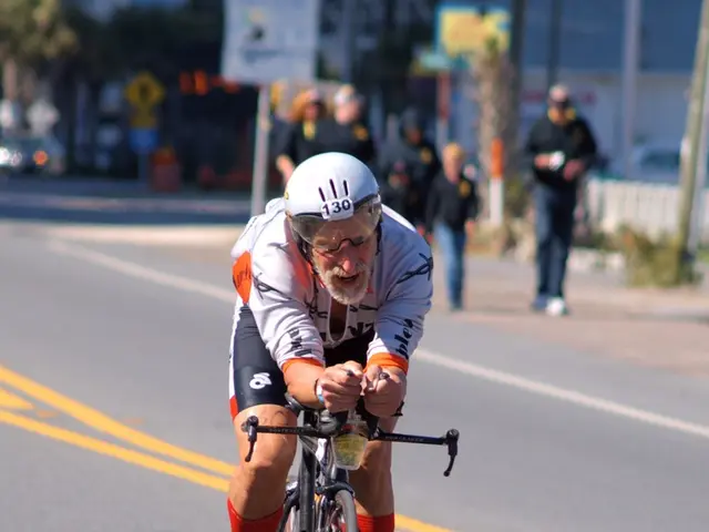 In this picture there is a old man riding a bicycle wearing a helmet on the road. In the...