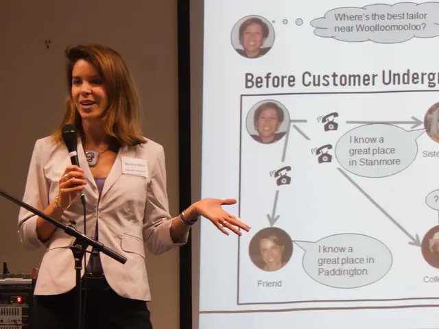 A lady with jacket is standing. She is holding a mic in her hand. And she is talking. To the left...