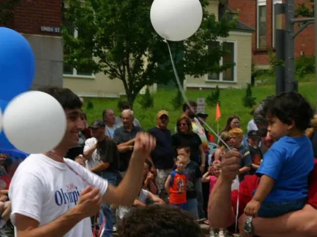 In this image there are a few people standing, one of them is holding a child and few are holding...