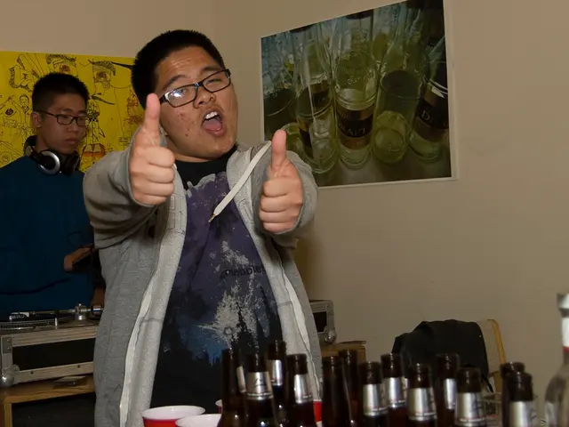 This picture is clicked inside the room. Man in blue t-shirt and grey jacket is standing in front...