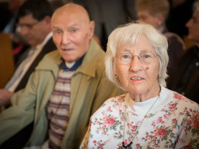 There is an old woman on the right side. Beside her there is an old man. In the background there...