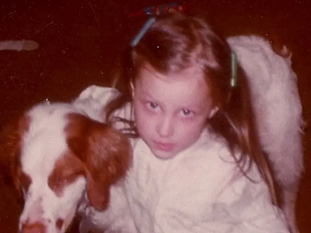 In this picture we can see a girl who is sitting on her knees. And there is a dog.