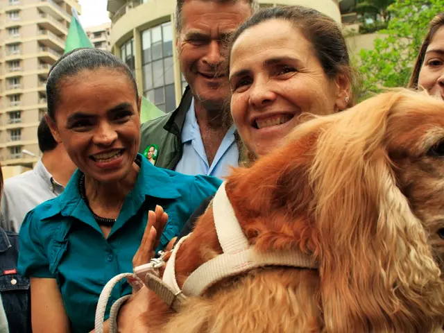 In this image I can see number of people where a woman is holding a dog, I can also see smile on...