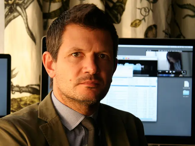 In this image we can see a man, he is wearing the suit, at back here is the computer, where is the...