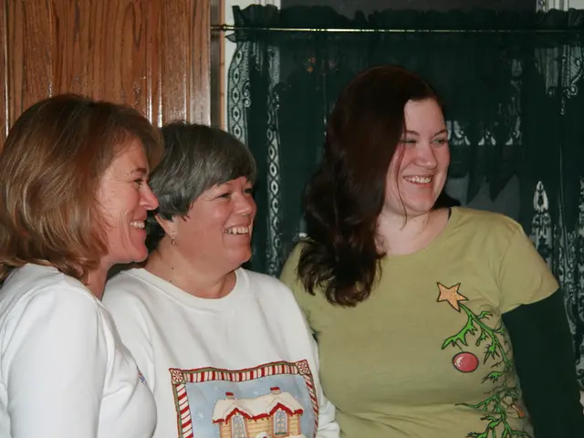 In the foreground of the image there are women standing and laughing. In the background of the...