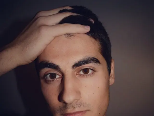 This is a close up image of a man, wearing clothes and the corners of the image are dark.