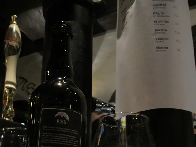 In this image, we can see bottles and there is a glass with drink and some papers are placed on the...