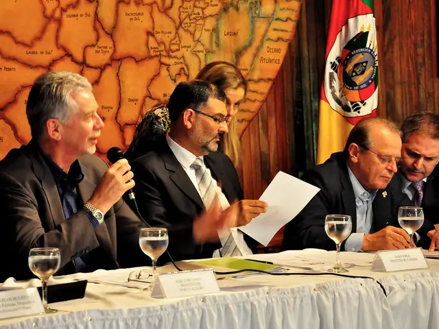 In this image we can see four men are sitting. They are wearing suits. One man is holding mic and...