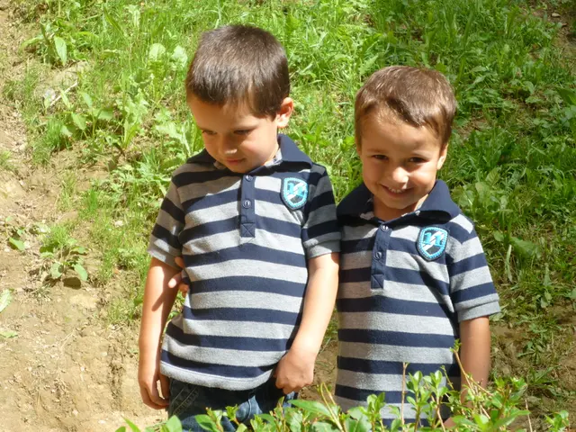 In this picture there are two boys who are wearing same dress. They are standing near to the plant....