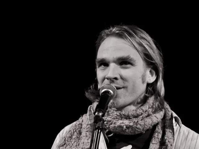 In the center of this picture we can see a person wearing a scarf and seems to be singing, we can...