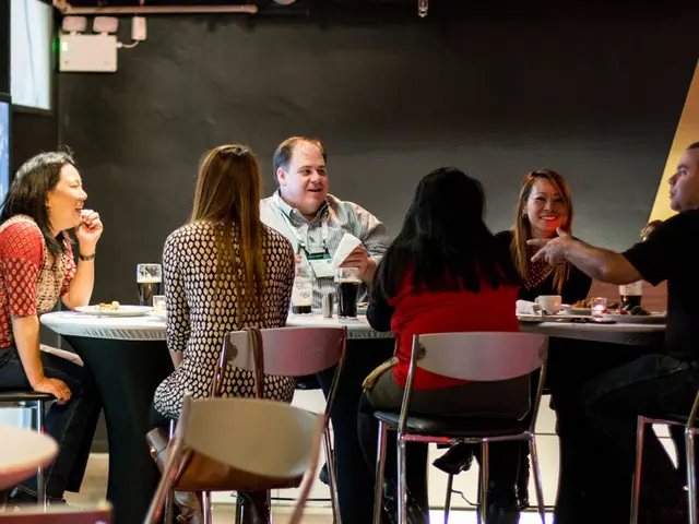 A group of people are sitting in chairs at a table. Of them four are women and three are men. There...