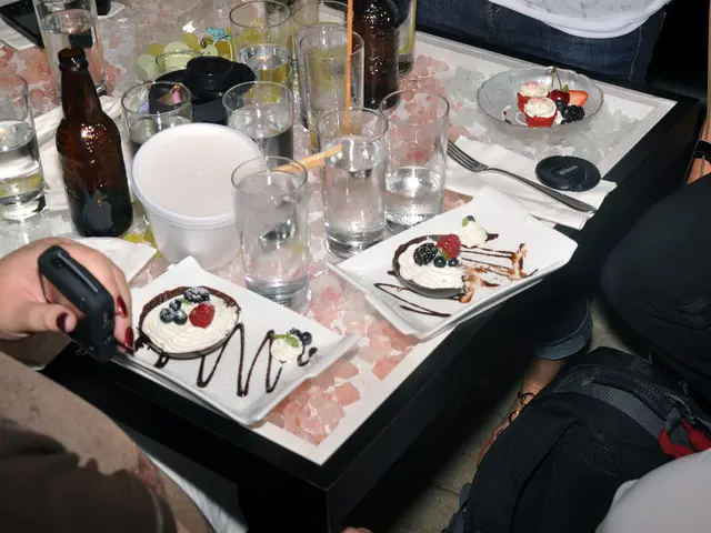 In this image I can see plate of food items, glasses, fork and glass bottles on a table. There is a...