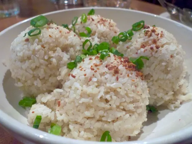 In this image we can see rice in a plate on a table and it is decorated with green veggie on it. In...