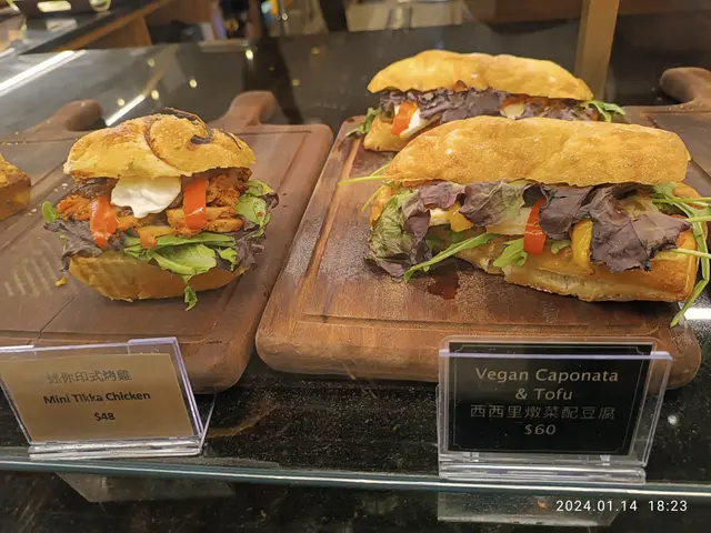 The image shows three vegan caponata and tofu sandwiches on wooden trays placed on a glass surface,...