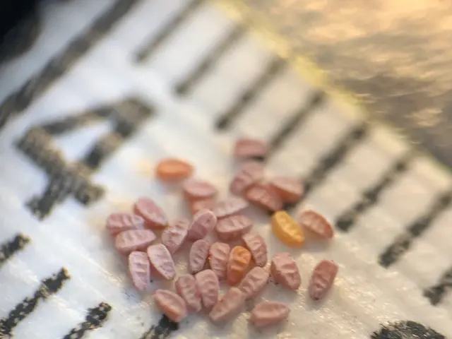 The image shows a close up of a piece of paper with a bunch of pills scattered across it. The pills...