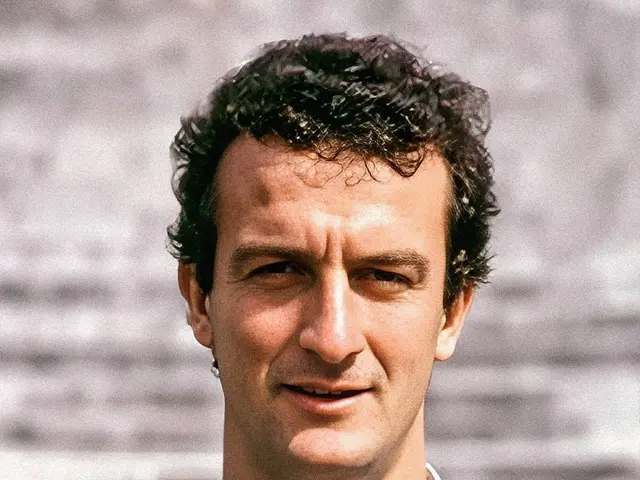 The image shows a man wearing a green t-shirt with a logo and text on it, standing in front of a...