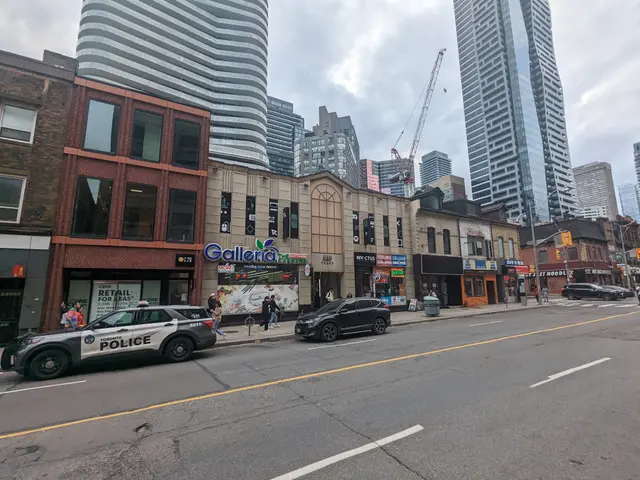 The image shows a police car parked on the side of a street in downtown Toronto, surrounded by tall...