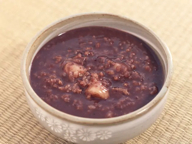 The image shows a bowl of black bean soup sitting on top of a table. The soup is a deep, dark brown...