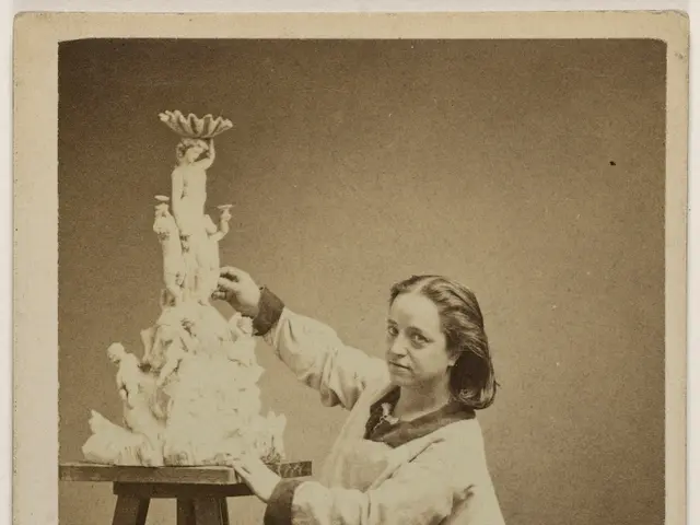 The image shows an old black and white photo of a woman standing and holding a cake on a table. At...